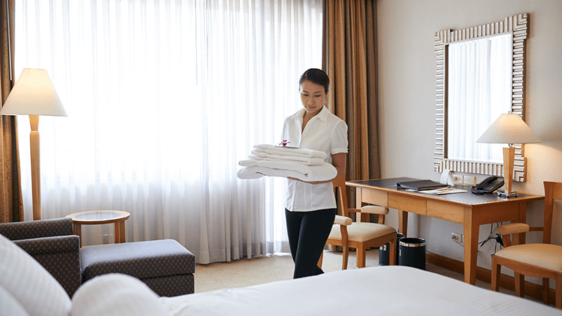 camareira levando as toalhas até a cama do quarto de hotel